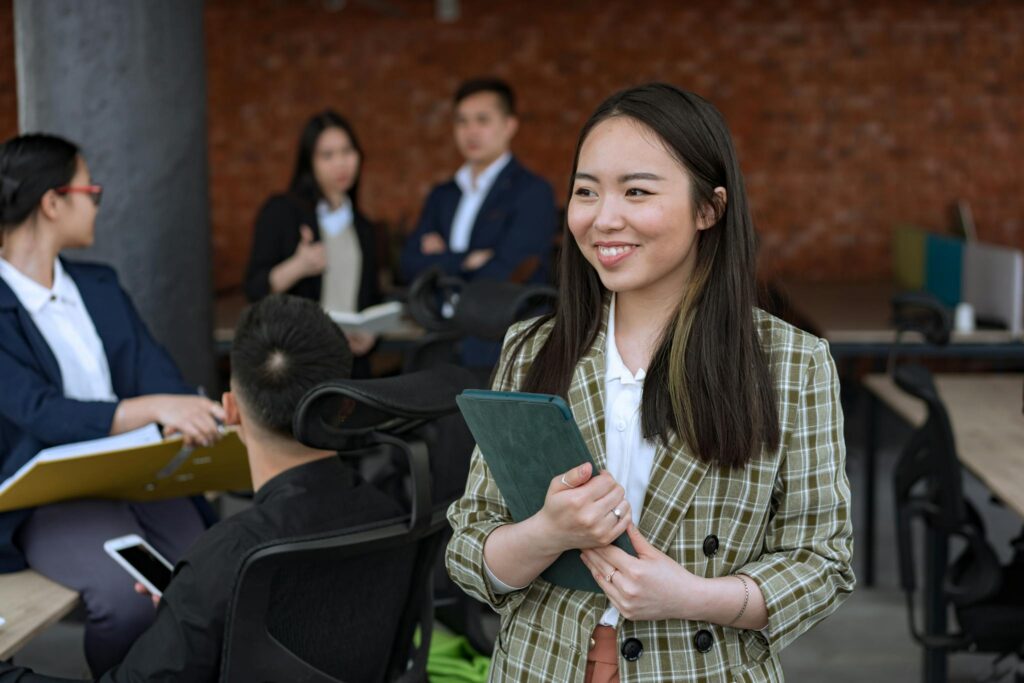 Smiling Asian woman holding tablet in a modern office setting, fostering collaboration.